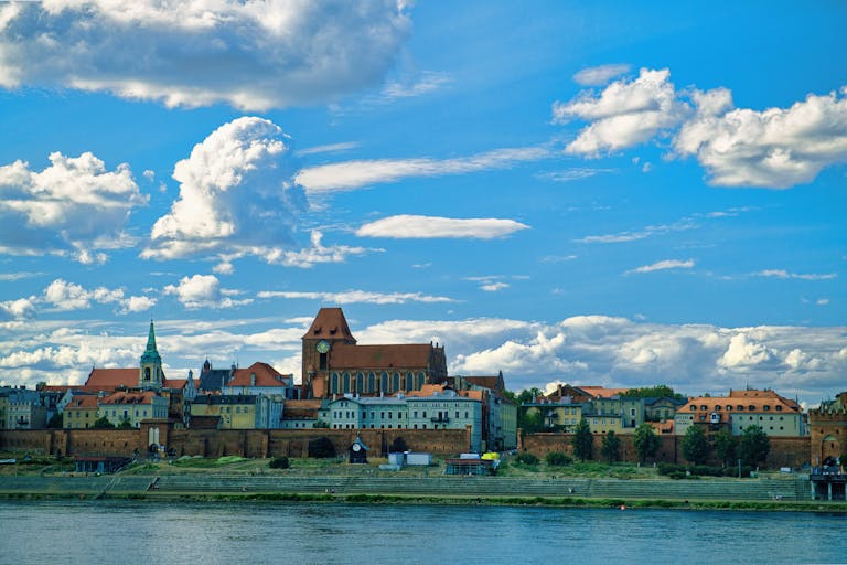 Beautiful view of Torun's old town by the river under a vibrant blue sky.