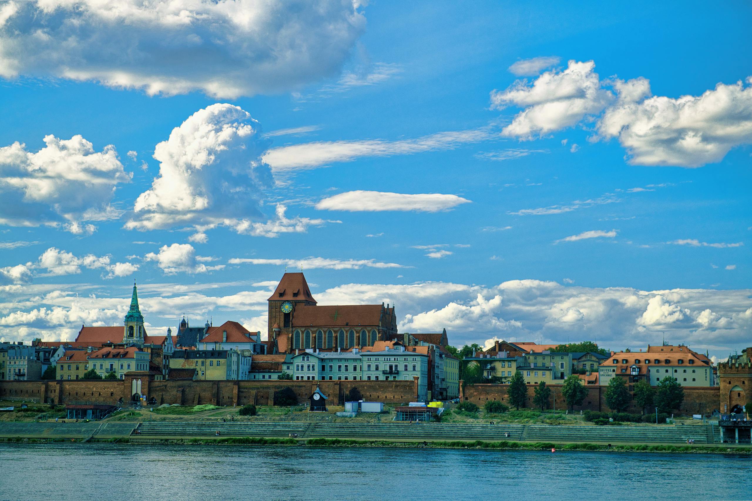 Beautiful view of Torun's old town by the river under a vibrant blue sky.