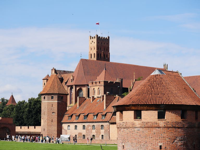 Explore the historic Malbork Castle with a clear blue sky backdrop in Pomeranian Voivodeship, Poland.