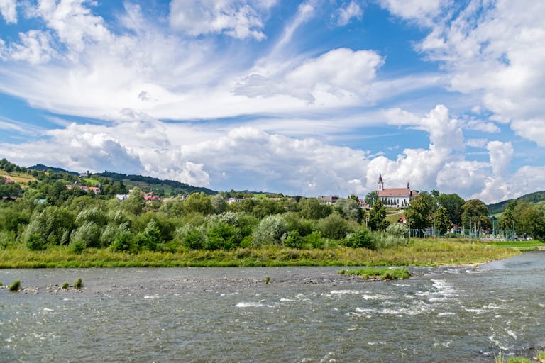 Idyllic summer scene with a church near a river under a dramatic cloudy sky in Poland.